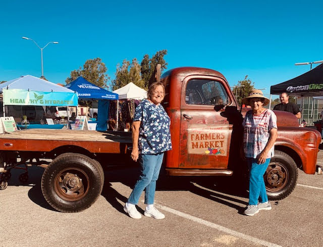 Becky Bauer and another woman standing in front of the High Desert Farmers Market pickup truck