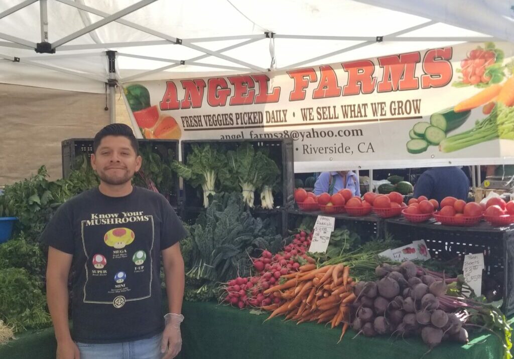 Aden Gaytan standing in front of his stand of vegetables
