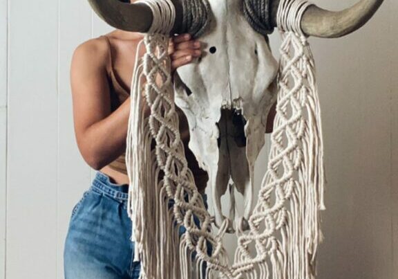 Woman standing holding a bull skull with crocheted art hanging from it
