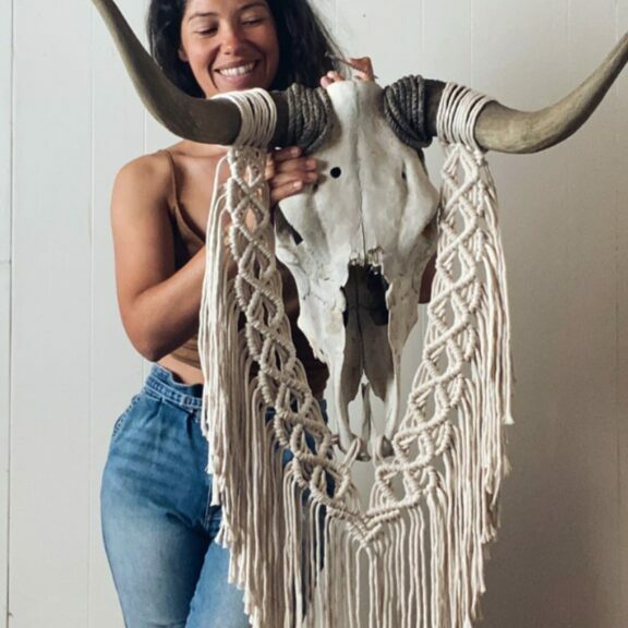 Woman standing holding a bull skull with crocheted art hanging from it