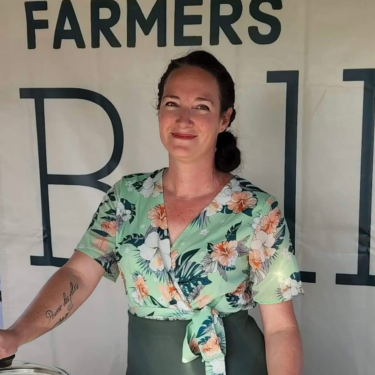 Chef Briggidy standing in front of a Farmers Belly sign and in front of a cooking pot